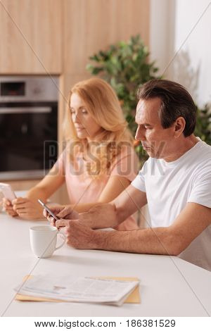 Lost in virtual world. Addicted unemotional skilled couple sitting at home and using smartphones while paying no attention to each other