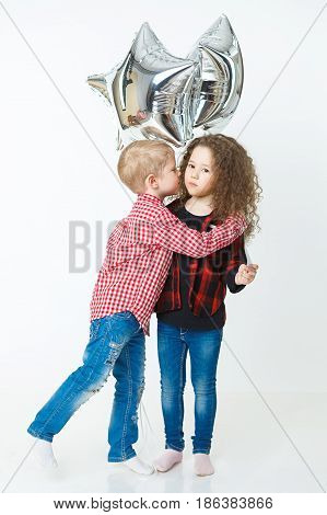 Little boy congatulate little curly girl, kiss, balloons. Studio