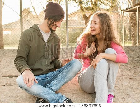 young couple sitting outdoors talking and smiling on sunny day. concept of modern  lifestyle fashionable indie friends or hipsters meeting and chilling out in freedom having fun leaisure time