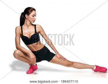 Fit woman stretching her leg to warm up - isolated over white background. 