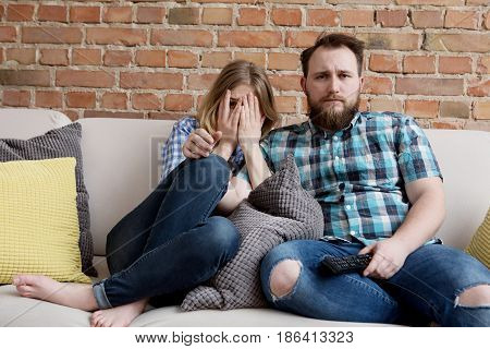 Young woman and man sitting on sofa and watching tv.