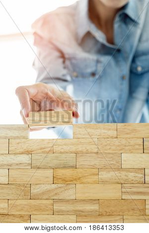 Hand Of Engineer Playing A Blocks Wood Tower Game (jenga) On Blueprint Or Architectural Project Conc