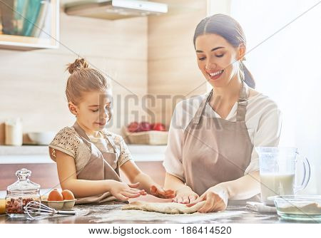 Happy loving family are preparing bakery together. Mother and child daughter girl are cooking cookies and having fun in the kitchen. Homemade food and little helper.