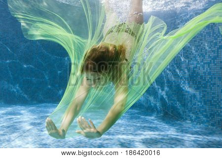 Woman dives with a fabric under the water in the pool.