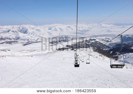 Empty cableway at winter day in Cahkadzor resort in mountains; Hrazdan town far away
