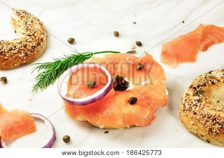 Bagel ingredients. Lox, purple onions, capers, dill, and the buns, shot on a white marble background in the process of making, with a place for text