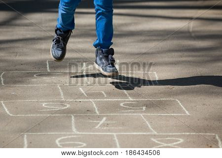 Closeup of boy's legs and hopscotch drawn on asphalt. Child playing hopscotch on playground outdoors on a sunny day. outdoor activities for children.