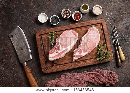 Raw pork meat with herbs, oil and spices on cutting board over dark background. . Top view
