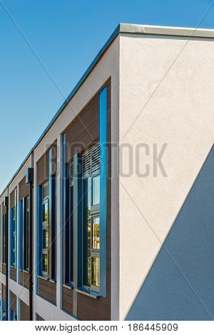 Corner detail of a modern white rendered building colourful blue and brown facade on a bright sunny day with clear sky. Abstract background.