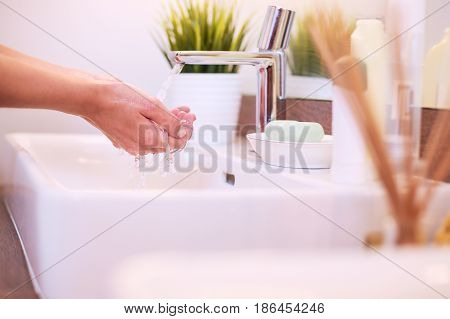 Young woman washing her face with clean water in bathroom.