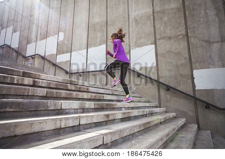 young sporty woman running upstairs on city stairs