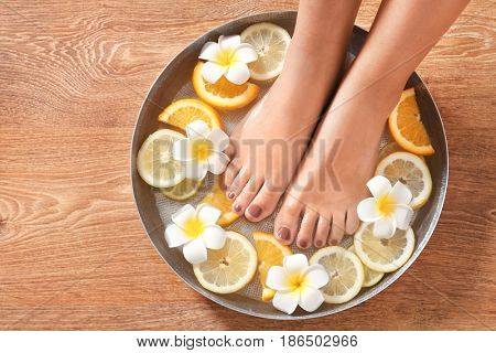 Female feet in spa bowl with citrus fruits on wooden background