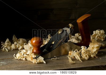 Woodworking hand planer tool on wooden boards in carpenter's workshop against dark brown background with copy space