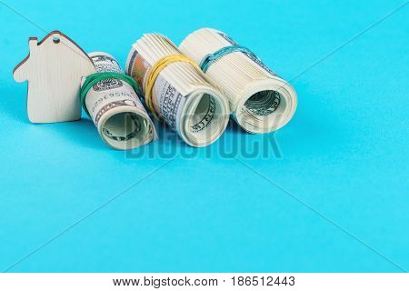 The concept of financial savings to buy a house. Mini model house dollars in rolls isolated on the blue background.