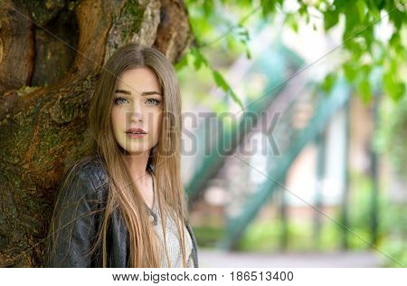 Young attractive woman hiding from the rain under a tree. Girl in rainy day, soft focus. Beautiful female face.