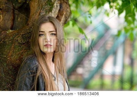 Young attractive woman hiding from the rain under a tree. Girl in rainy day, soft focus. Beautiful female face.
