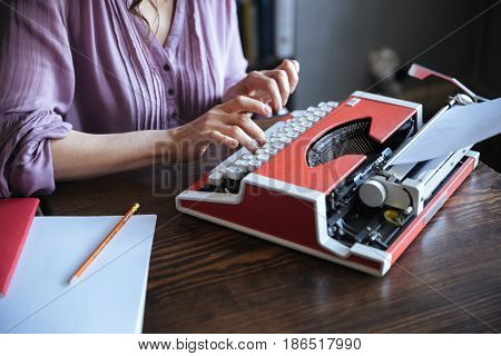 Cropped image of an authoress sitting at the table and typing on typerwriter indoors