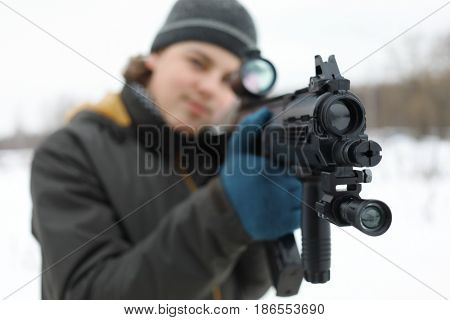 Teenager with gun takes aim during lasertag game outdoor at winter, focus on muzzle