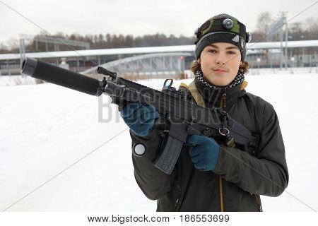 Boy pose with gun during lasertag game outdoor at winter day near railway station