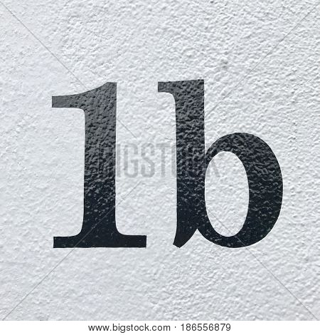 Number 1b house number letter address sign painted black on white stone wall textured background