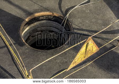 cable layout into a sewer well on the asphalted road enclosured by railings showing attention sign