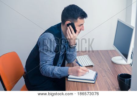 An office worker works at a computer in the office and takes an order by phone. Office concept with working environment.