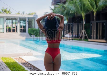 Young sexy woman in swimsuit stand near poolside wearing sunglasses at luxury hotel.