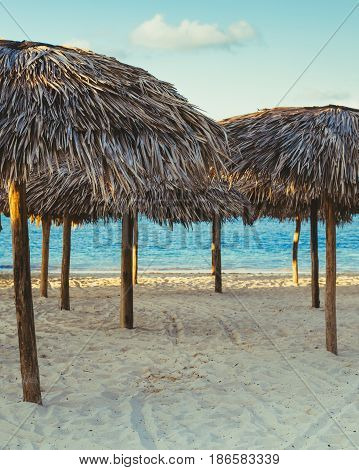 Group row of many thatch attap straw umbrellas covers standing on sea ocean beach at sunset toned with filters in retro vintage film style summer vacation landscape