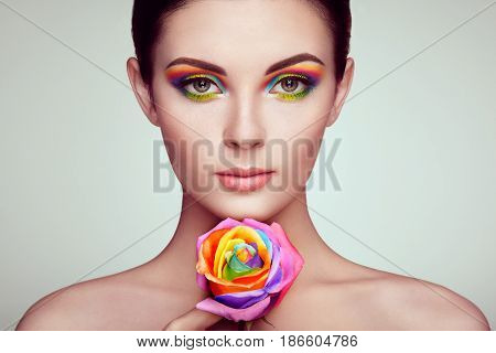 Portrait of beautiful young woman with rainbow rose. Bright colors. Long eyelashes vivid colorful eyeshadows. Rainbow make up. Multicolored flowers