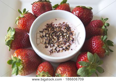 Greek strawberry yoghurt in a bowl with a superfruit topping of dried blueberries, hibiscus, chia seeds and airy quinoa pops surrounded by delicious strawberries