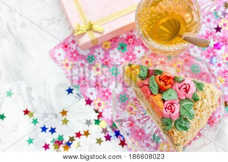 Piece of birthday cake tea in cup gift box and colorful confetti on table top view