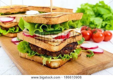 Multilayered sandwiches with a juicy cutlet cheese radish cucumber lettuce arugula on a cutting board on a white wooden background.