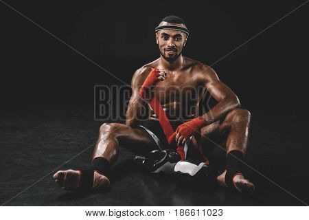 Smiling Muay Thai Fighter Swathing Hand In Bandage Isolated On Black