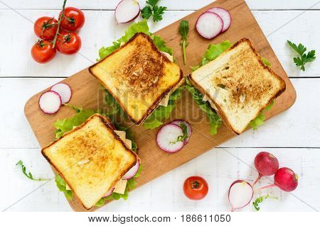 Multilayered sandwiches with a juicy cutlet cheese radish cucumber lettuce arugula on a cutting board on a white wooden background. Top view.