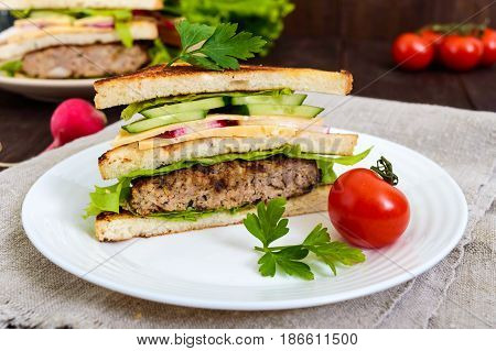 Multilayered sandwiches with a juicy cutlet cheese radish cucumber lettuce arugula cutting in half on a plate on a dark wooden background. Close up