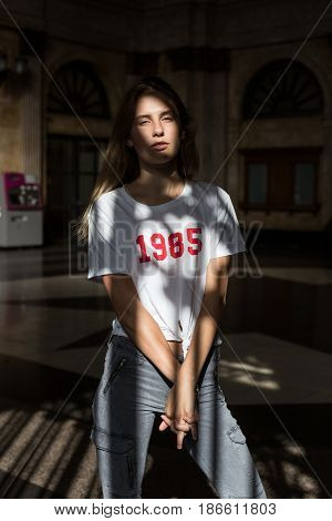 Feminine tall fashion model poses for professional photoshoot outside in urban city with dramatic beautiful shadow falling on her face