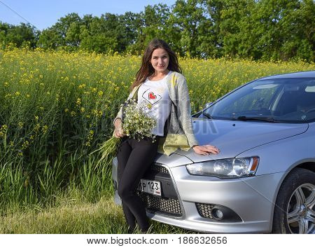 A Beautiful Young Woman With A Bouquet Of Daisies Stands Near A Silver Car