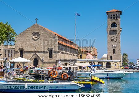 RHODES GREECE - JULY 4 2015: Tourists walking on quay of Mandraki harbour near Church of the Evangelismos (Annunciation)