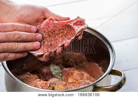 Close up of chefs hands spicing the meat. Casserole with raw meat on a white background.