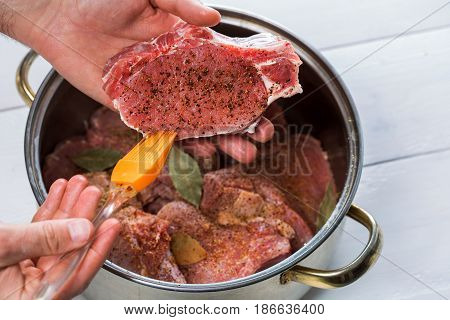Close up of chefs hands spicing the meat. Casserole with raw meat on a white background.