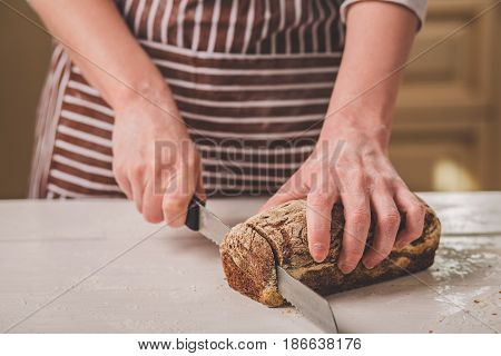 Woman cutting bread on wooden board. Bakehouse. Bread production. A woman in a striped apron