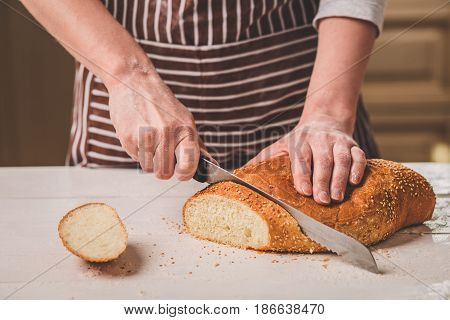 Woman cutting bread on wooden board. Bakehouse. Bread production. A woman in a striped apron