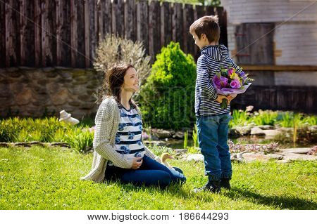 Young pregnant woman receiving bouquet of colorful flowers from her child for Mothers Day sitting in a beautiful spring blooming garden. Mother's day concept