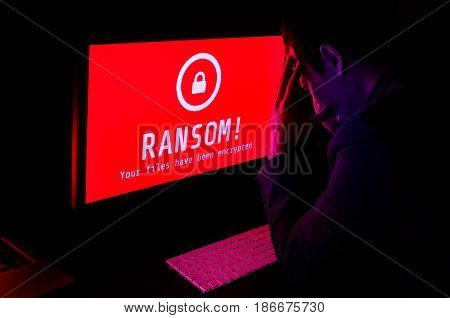 Computer screen with ransomware attack file encrypted alerts in red and a man in suit get stress with keyboard in a dark room ideal for online security failure and digital crime long exposure selective focus