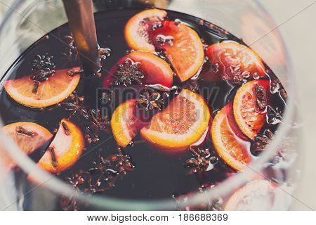 Making hot alcohol, mulled wine for sale at country fair. Glintwine from red wine with citrus and cloves in big metal stock pot, mixed with soup ladle. Closeup