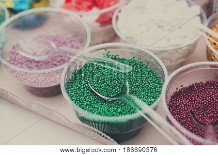 Ice cream treats and toppings sale. Rainbow sprinkles, stars, non pareil and glitter cupcake decorations, bright green. Closeup in plastic plates with spoons. Confectionery store