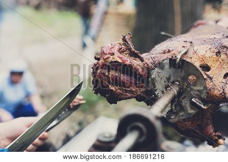 Barbecue picnic at country fair. Lamb roasted at spit closeup. Grill, big piece of meat at rolling skewer. Street vendor, professional chef hands cooking bbq food. Catering concept, vertical