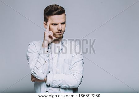 Focused serious man standing in front of camera. Attractive guy holding his right hand at forehead and deeply thinking about something. Isolated. Close up
