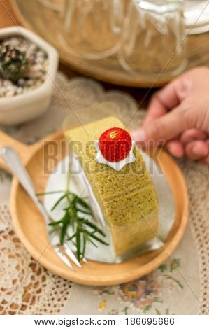 Hand holding wooden plate of matcha green tea cake with fork rosemarry over vintage table cloths.