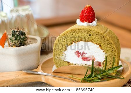Hand holding wooden plate of matcha green tea cake with fork rosemarry over vintage table cloths.
